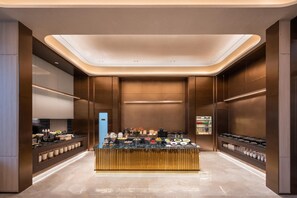 Eine moderne Hotelhalle mit einer zentralen Büfett-Ecke, einer Rezeption und einem großen Spiegel.