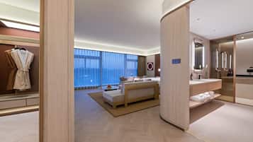 A modern hotel room with a large bed, a sitting area, and a bathroom with a mirror and sink.