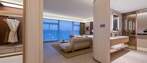 A modern hotel room with a large bed, a sitting area, a bathroom with a mirror and shower, and a view of the city through large windows.
