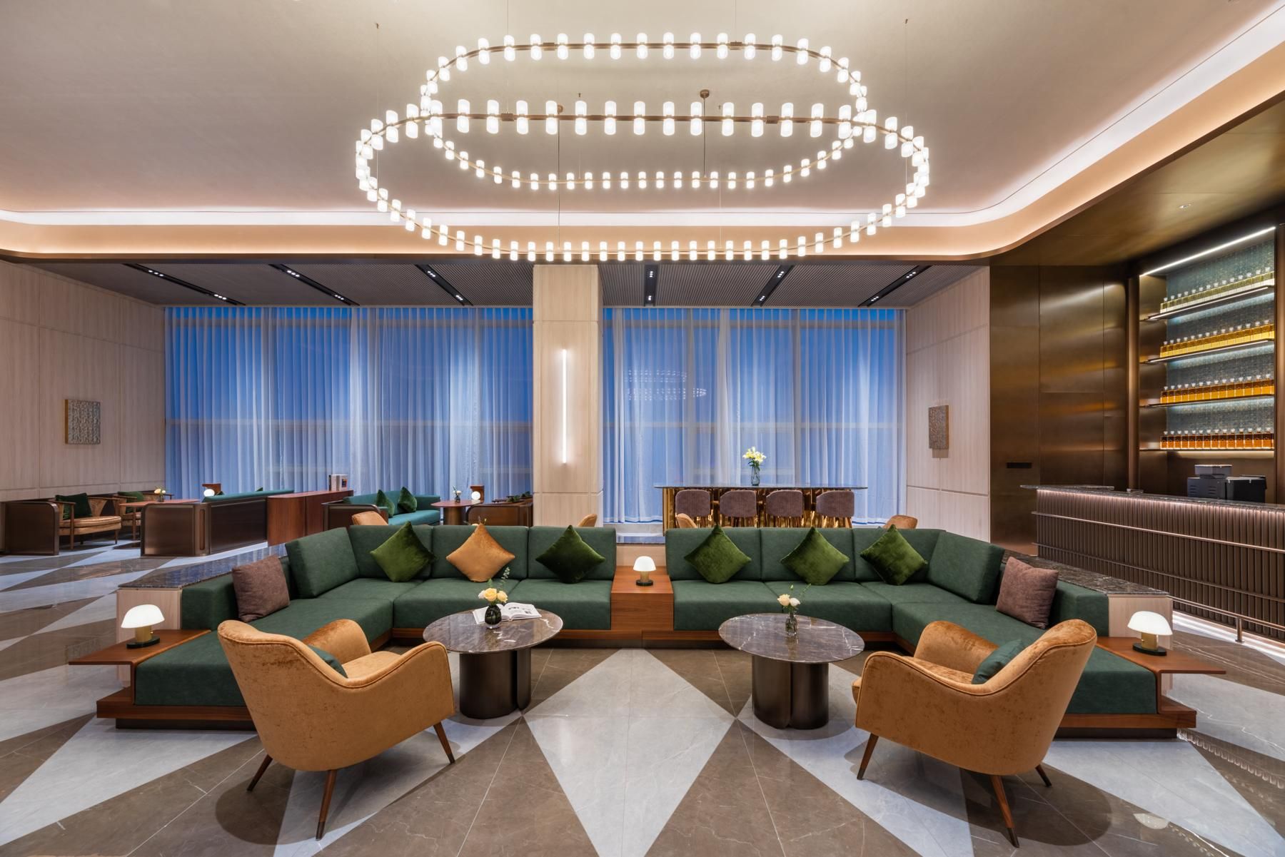Un espacio lounge moderno con un sofá verde, dos mesas redondas y una lámpara circular original.