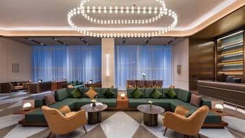 A modern lounge area with a green sofa, two round tables, and a unique circular light fixture.