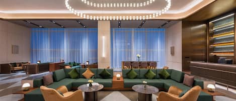 Un espacio lounge moderno con un sofá verde, dos mesas redondas y una lámpara circular original.