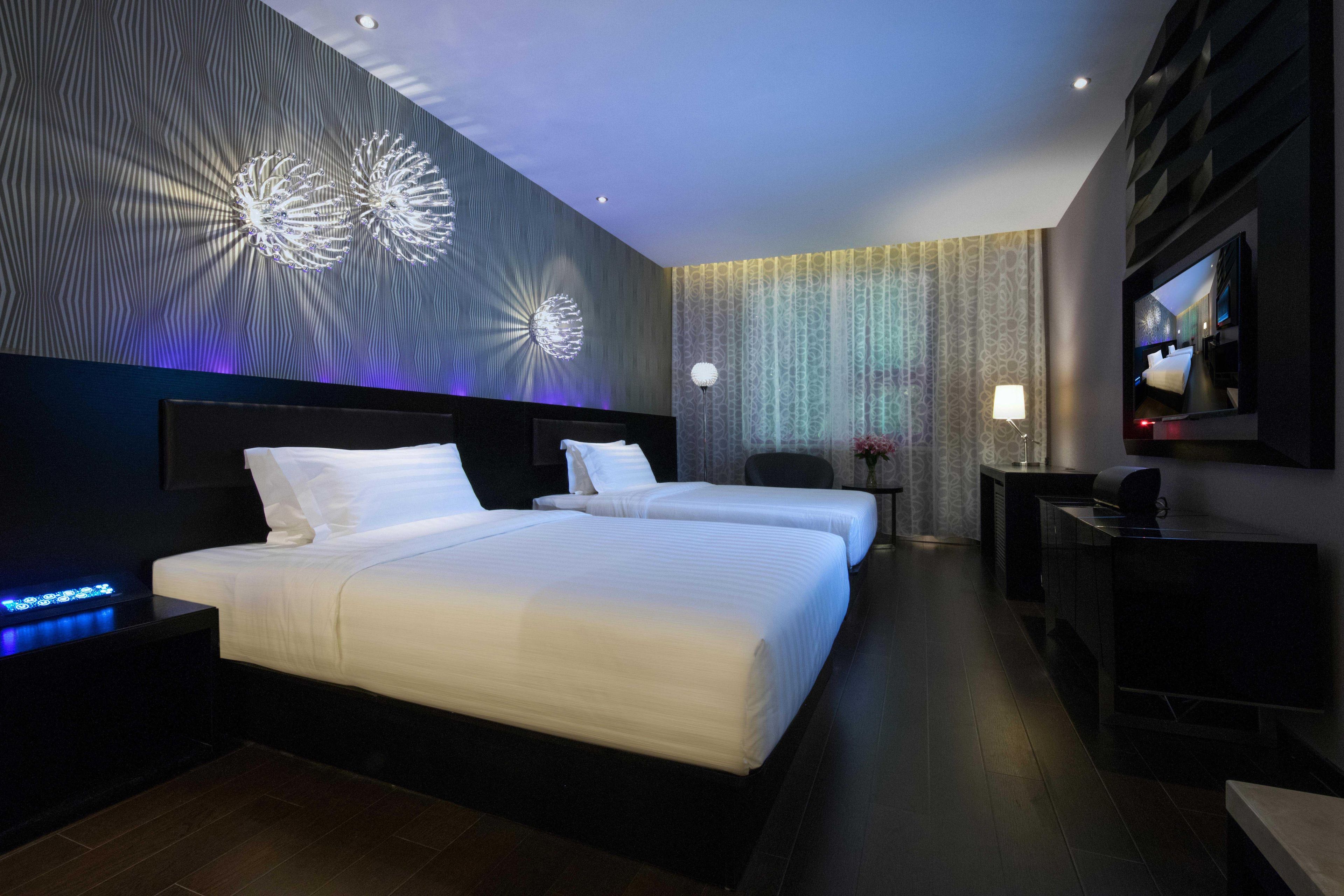 A hotel room with two beds, a TV, a desk, and a wall with a light projection.