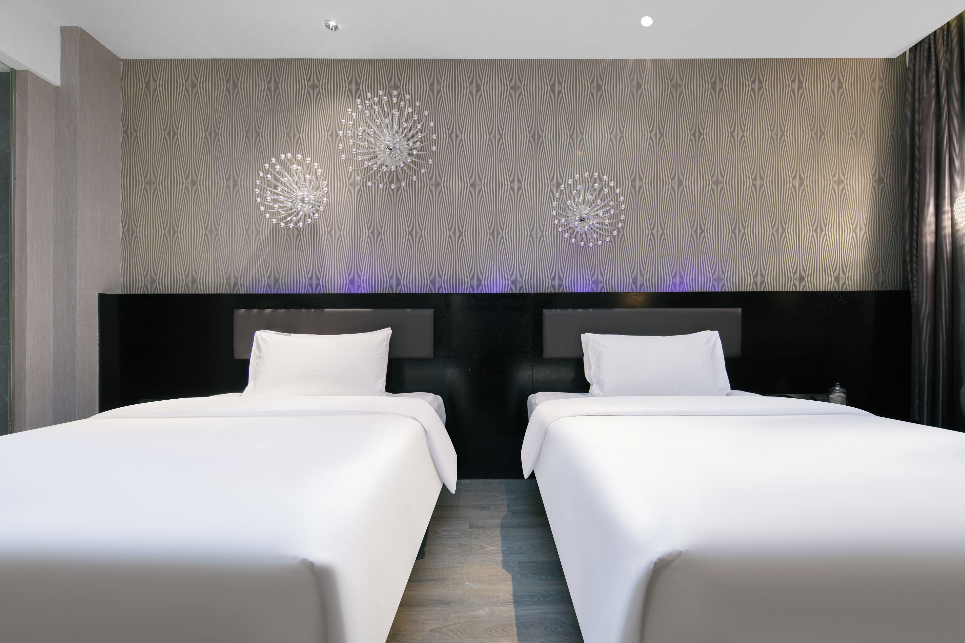 A hotel room with two beds, a patterned wallpaper, and a chandelier.
