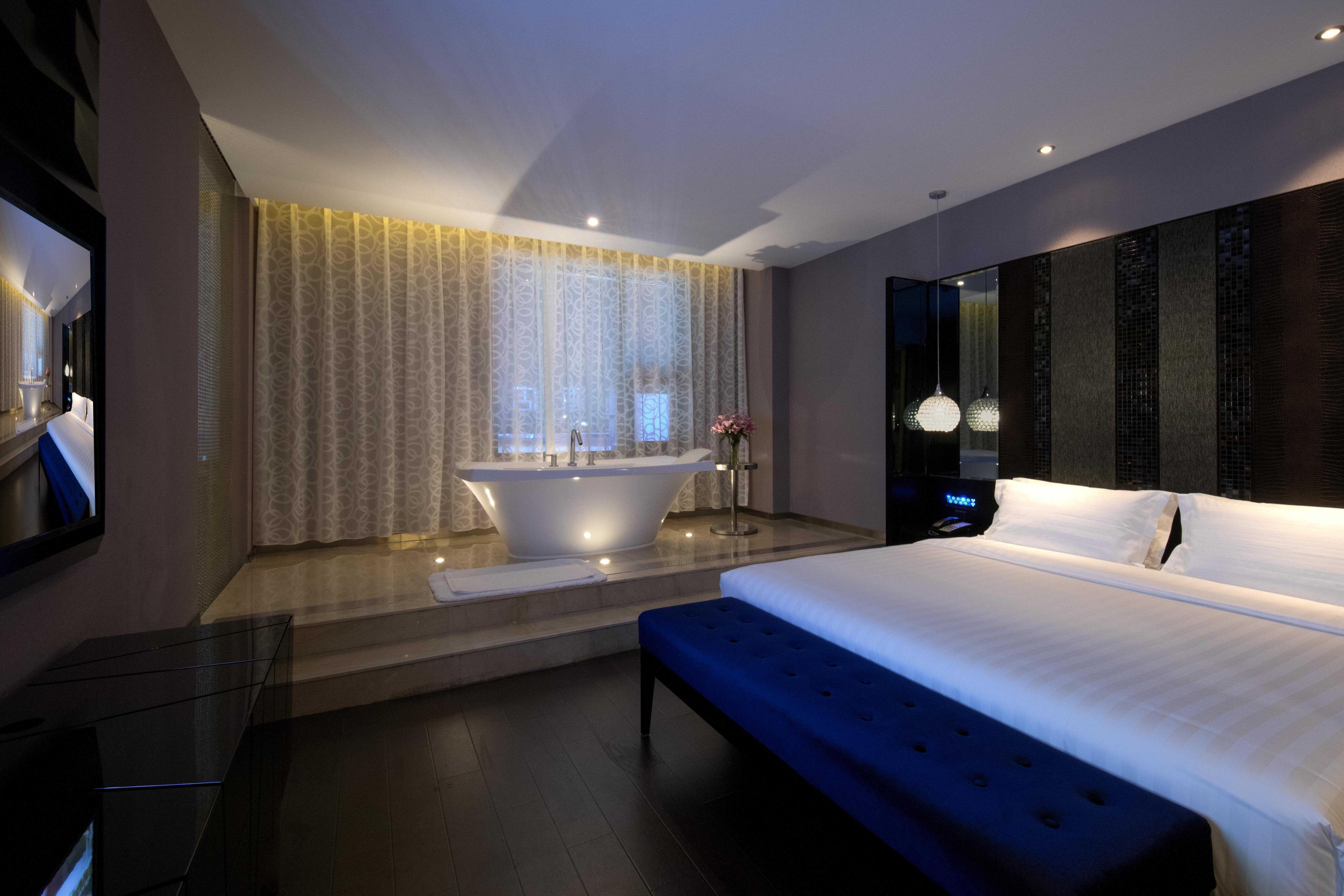 A modern hotel room with a large bed, a bathtub, and a large mirror.