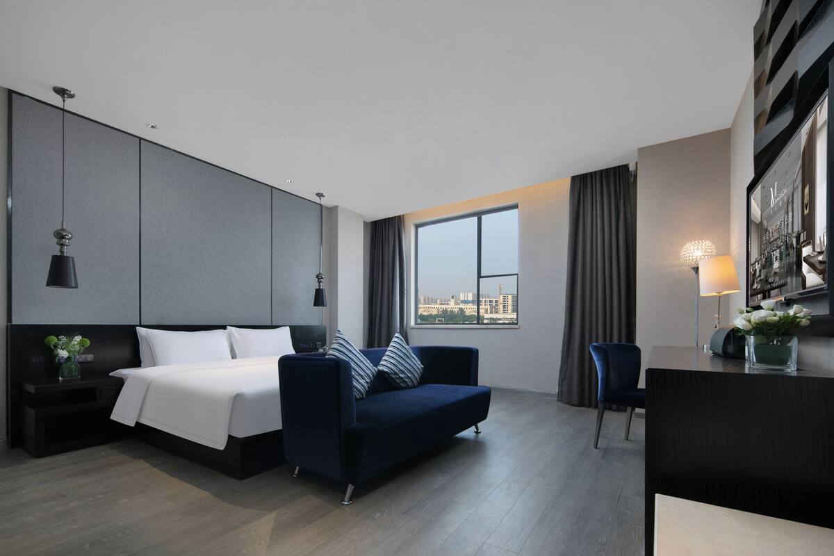 Una habitación de hotel moderna con cama, sofá, escritorio y un ventanal con vistas a la ciudad.