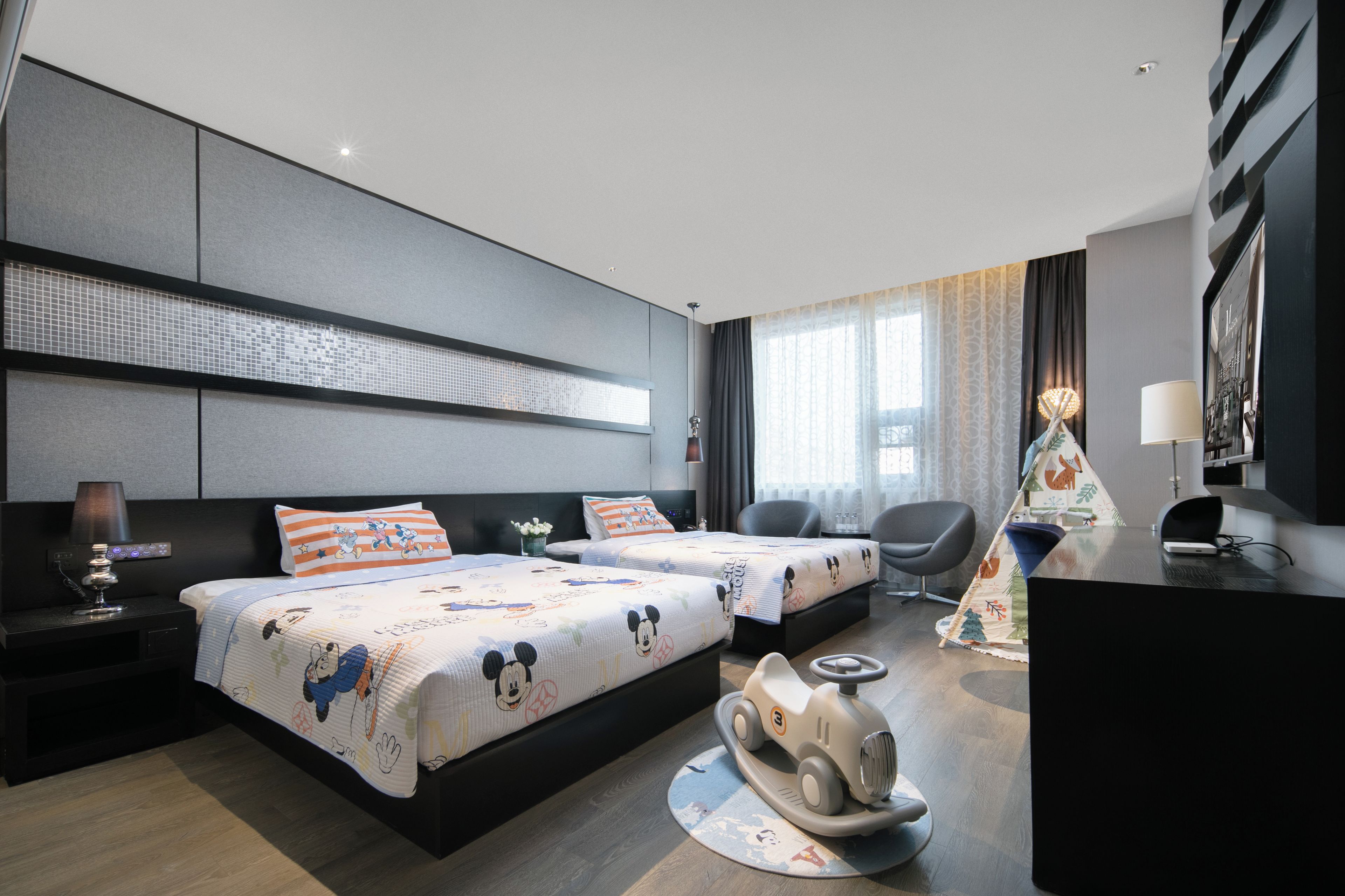 A hotel room with two beds, a desk, a chair, a lamp, and a decorative wall panel.