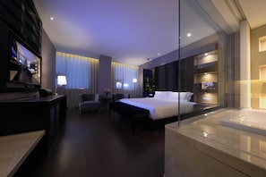 A modern hotel room with a large bed, a desk, a chair, a small table with a lamp, and a glass partition. - Crystal Orange Hotel Taizhou Maoye Tiandi (Taizhou)