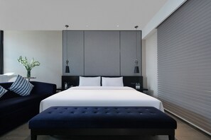 A modern hotel room with a large bed, a dark blue sofa, a small table with a vase, and a large window with blinds. - Crystal Orange Hotel Taizhou Maoye Tiandi (Taizhou)
