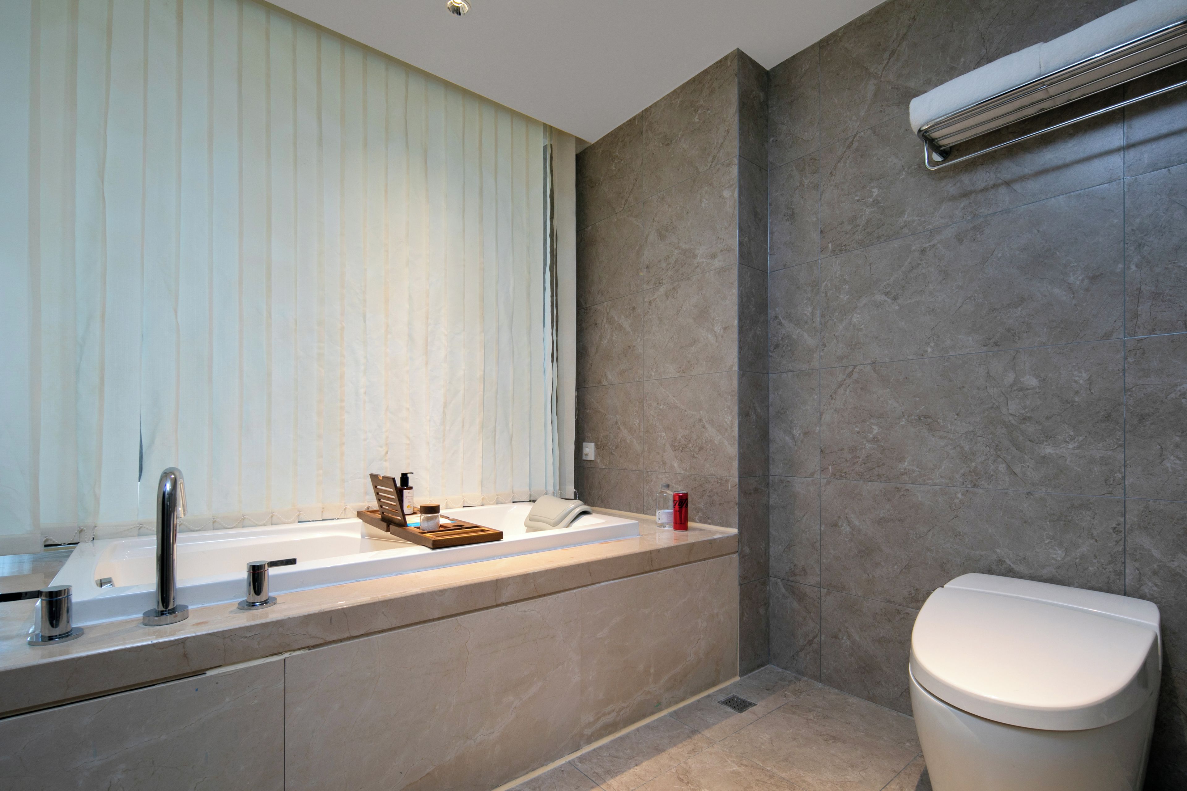 Un baño moderno con bañera, inodoro y ventana con persianas.