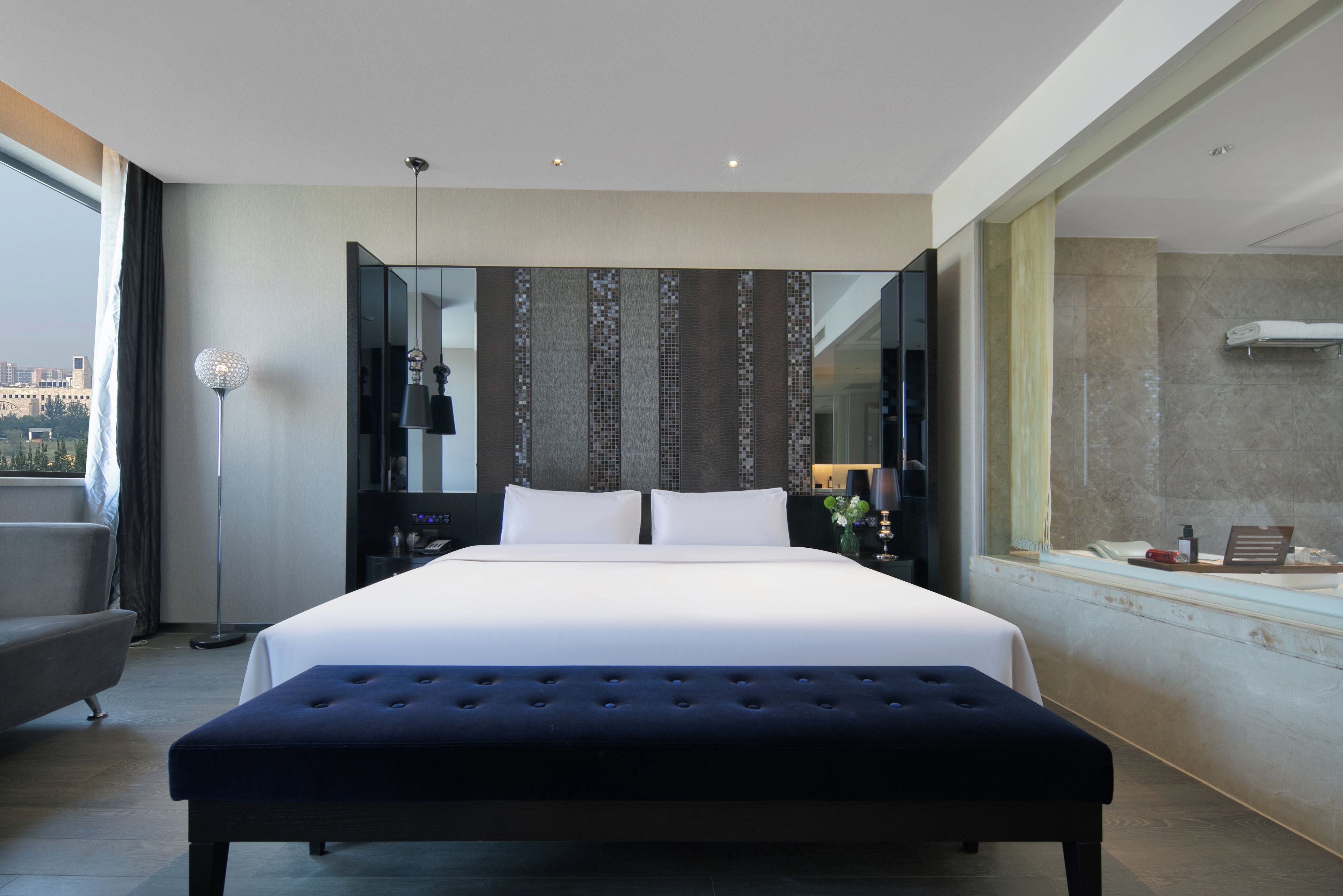 Quarto de hotel moderno com uma cama grande, área de estar, uma janela ampla e banheiro com banheira.