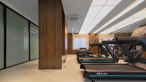 Un gimnasio con cintas de correr, un pilar de madera y un ventanal grande.