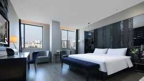 Una habitación de hotel moderna con una cama grande, un escritorio, una silla y vistas a la ciudad.