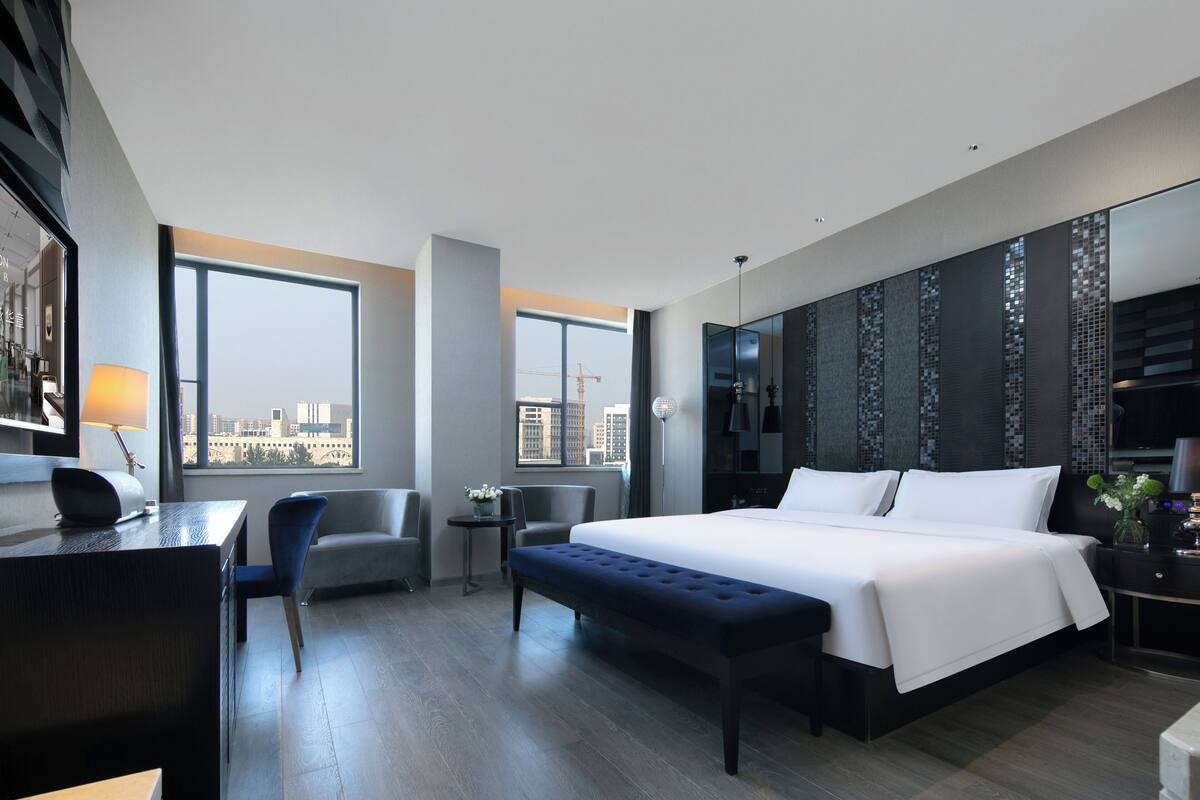 Una habitación de hotel moderna con una cama grande, un escritorio, una silla y vistas a la ciudad.