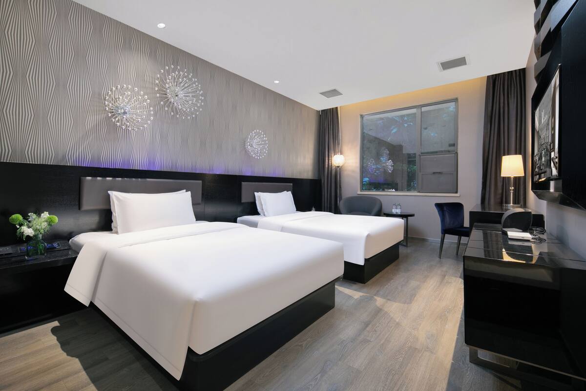 Una habitación de hotel moderna con dos camas, un escritorio, una silla, un ventanal grande y decoración en la pared.