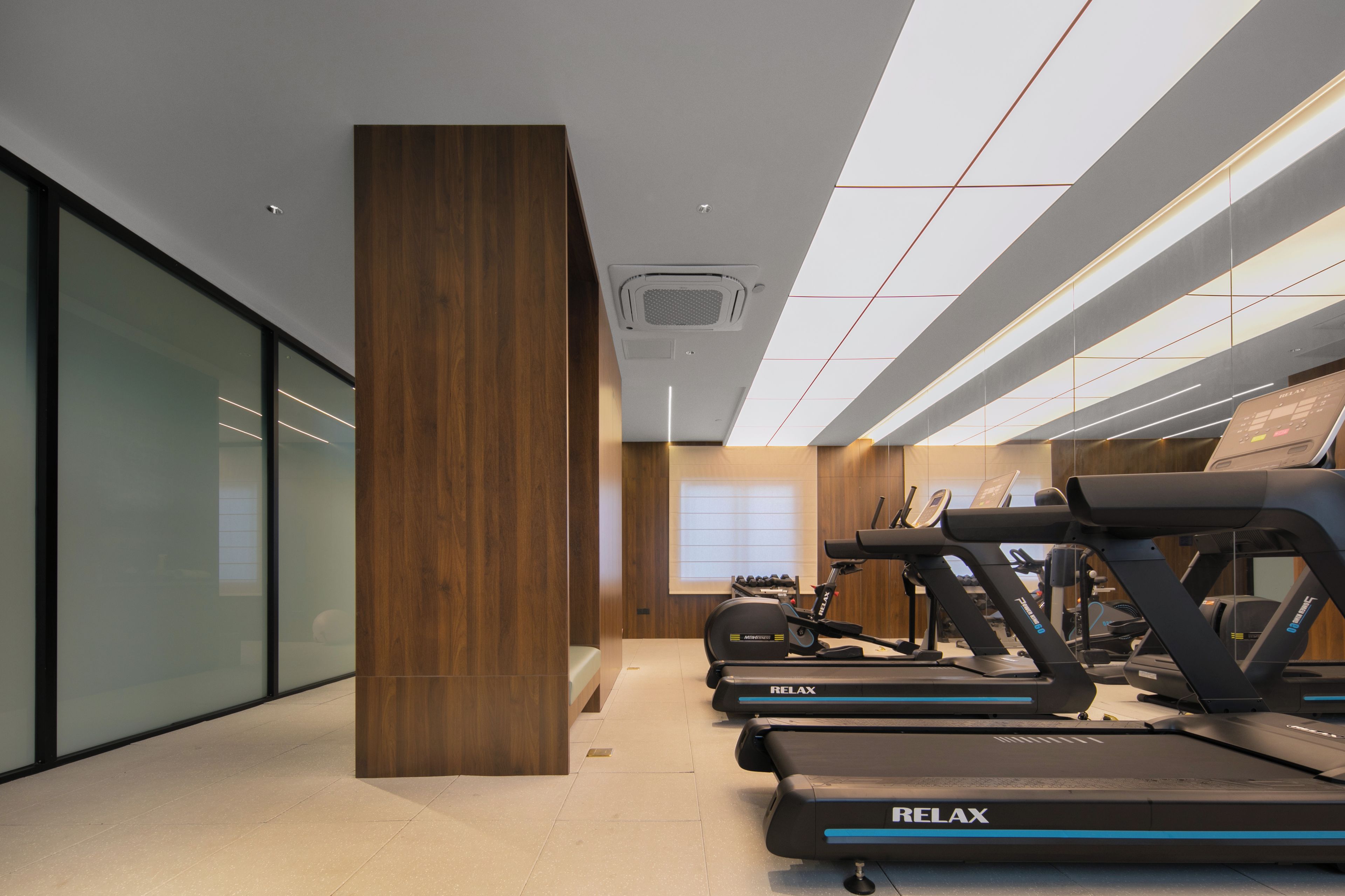 Un gimnasio con cintas de correr, un pilar de madera y un ventanal grande.