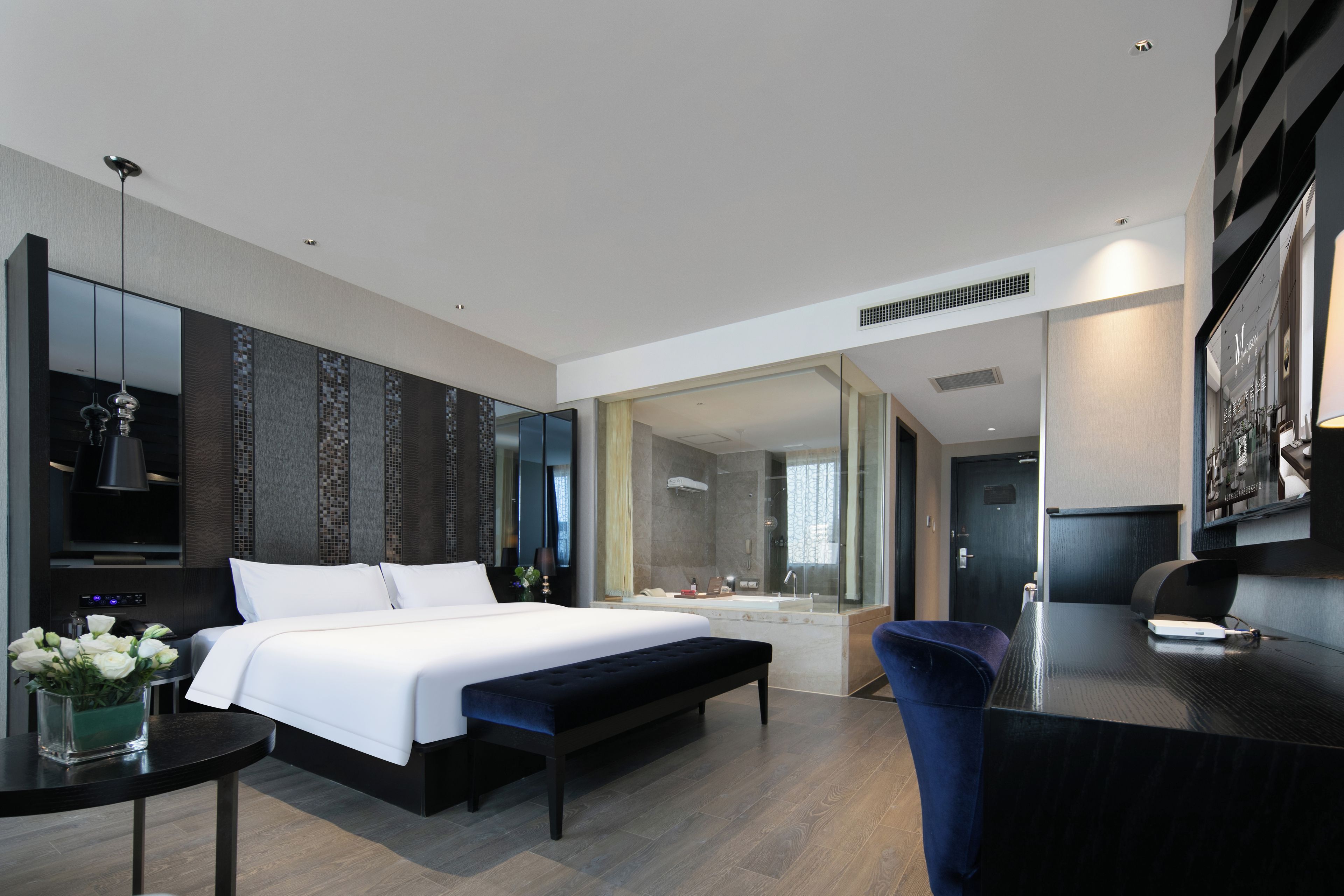 Una habitación de hotel moderna con una cama grande, un escritorio, un baño con bañera y un espejo amplio.