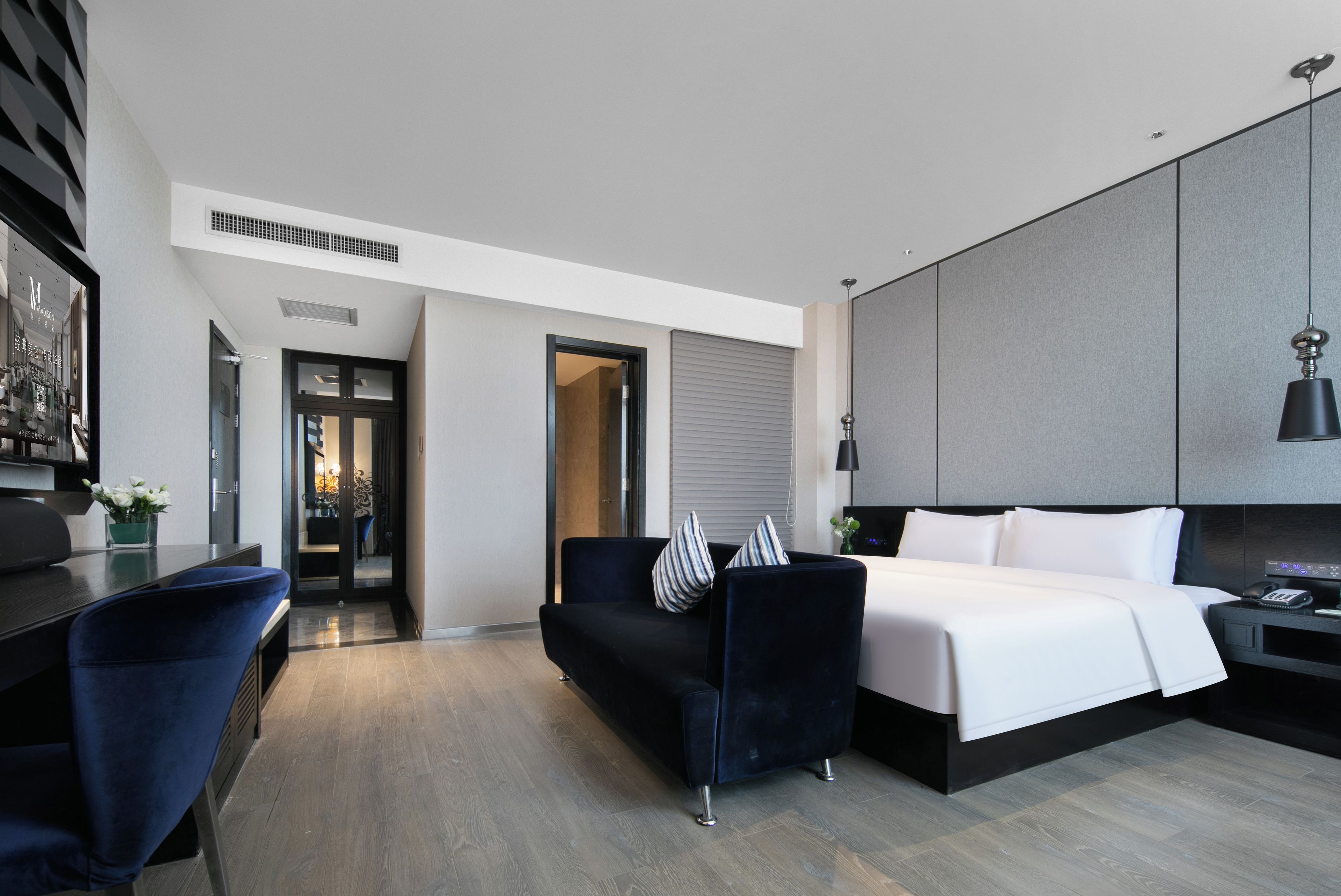A modern hotel room with a bed, a desk, a sofa, and a wardrobe.