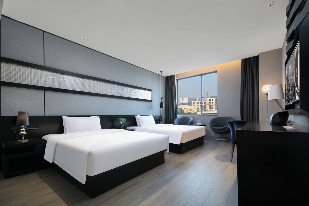 Habitación de hotel moderna con dos camas, un escritorio, una silla y un amplio ventanal con vistas a la ciudad.