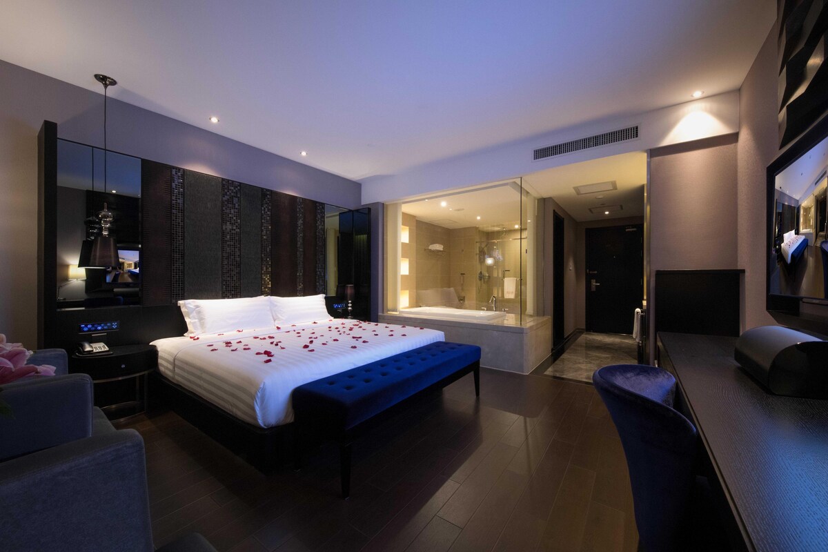 A modern hotel room with a large bed, a separate bathroom, and a desk area.