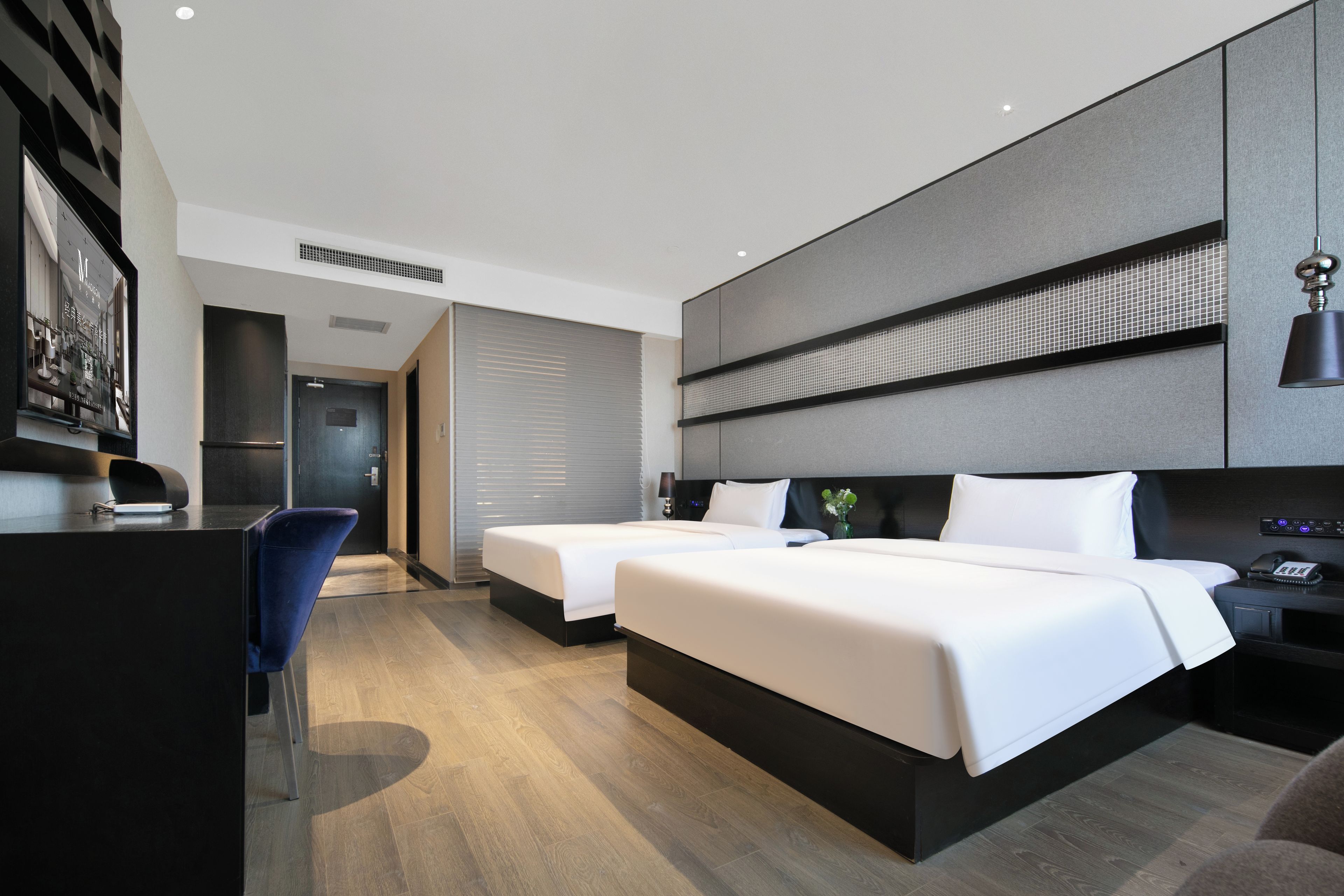 Ein modernes Hotelzimmer mit zwei Betten, einem Schreibtisch und einem Sessel.