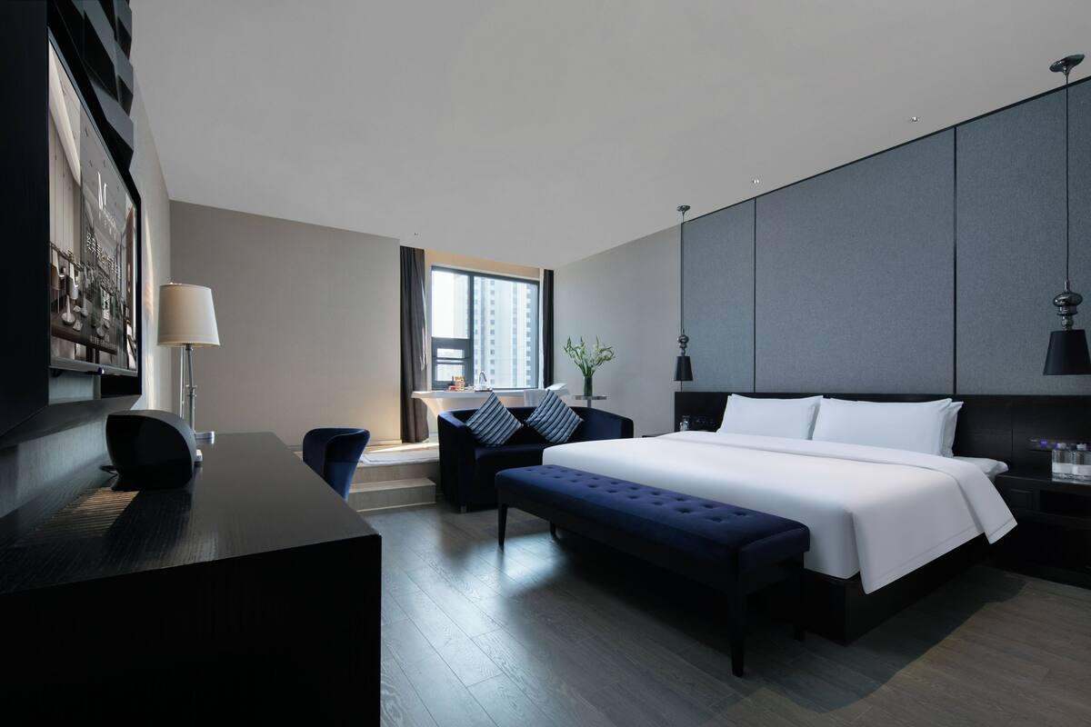 Una habitación de hotel moderna con una cama grande, un escritorio, una silla y vistas a la ciudad.