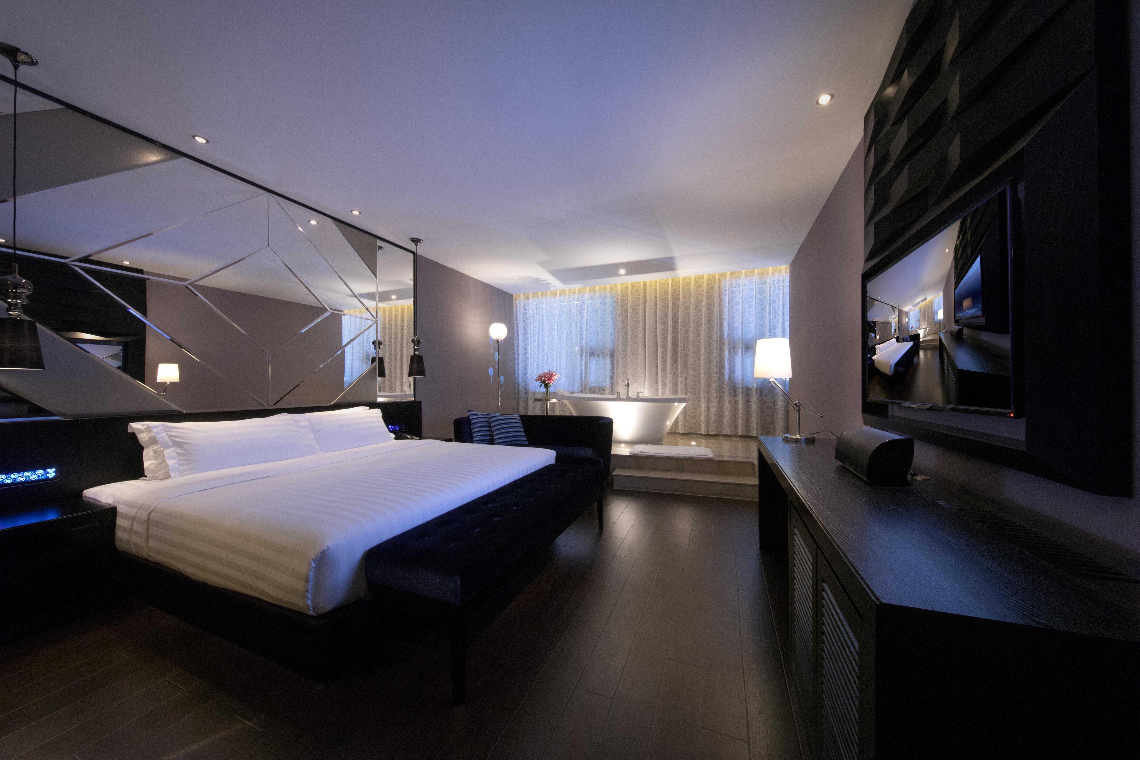 Une chambre d’hôtel moderne dotée d’un grand lit, d’un bureau, d’une télévision à écran plat et d’une salle de bain visible à travers une paroi en verre.
