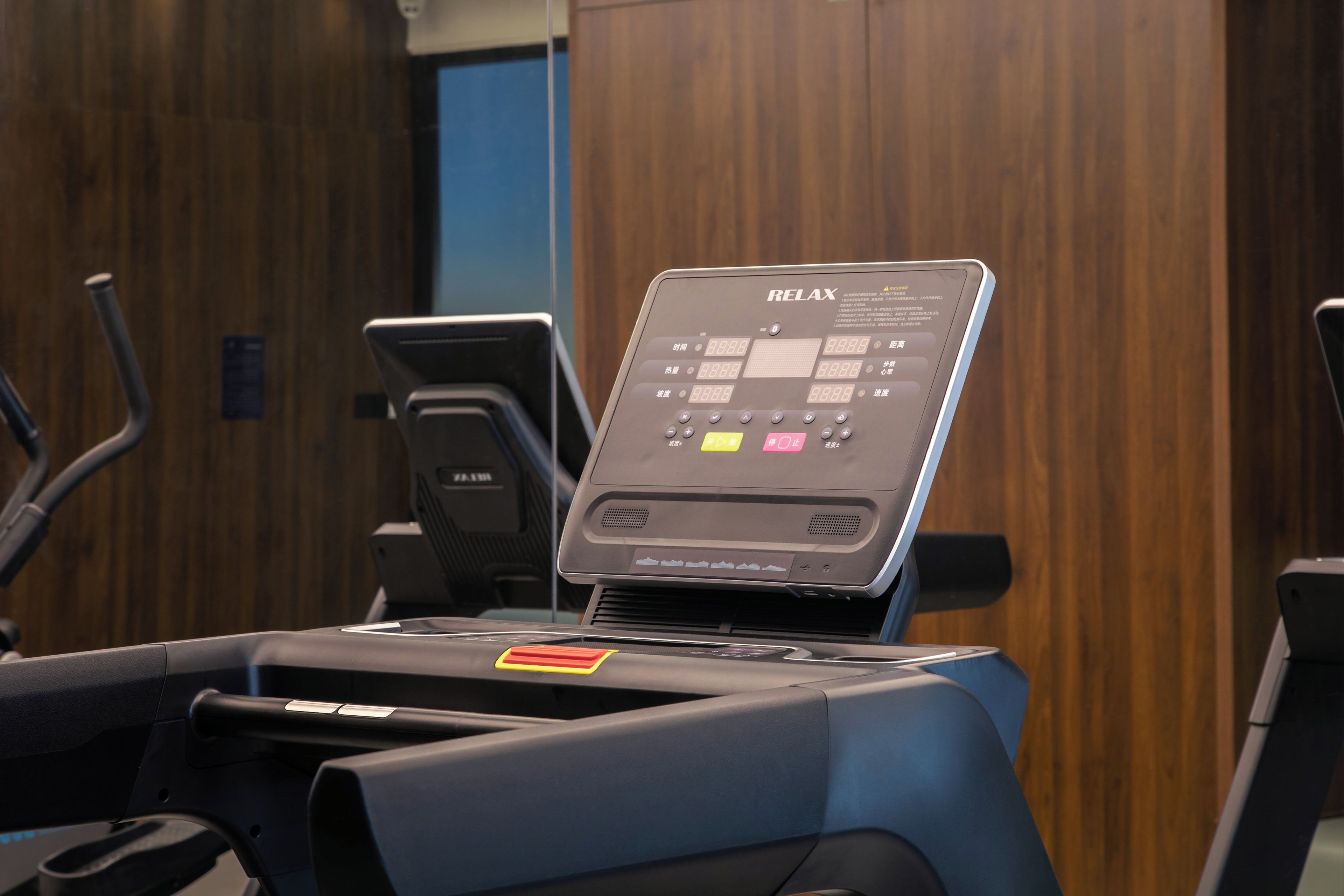 A treadmill with a control panel, a water bottle holder, and a wooden wall in the background.