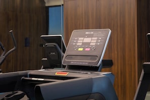 A treadmill with a control panel, a water bottle holder, and a wooden wall in the background.