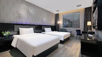 A modern hotel room with two beds, a desk, a chair, a large window, and decorative wall art.