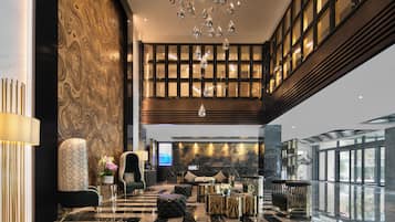 A spacious lobby with a high ceiling, a marble floor, and a seating area with a sofa and armchairs.