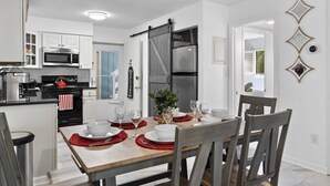 Una cocina moderna con armarios blancos, un refrigerador negro y una zona de comedor con una mesa de madera para cuatro comensales.