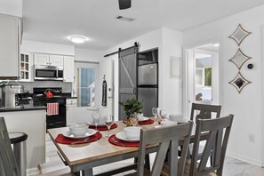 Una cocina moderna con armarios blancos, un refrigerador negro y una zona de comedor con una mesa de madera para cuatro comensales.