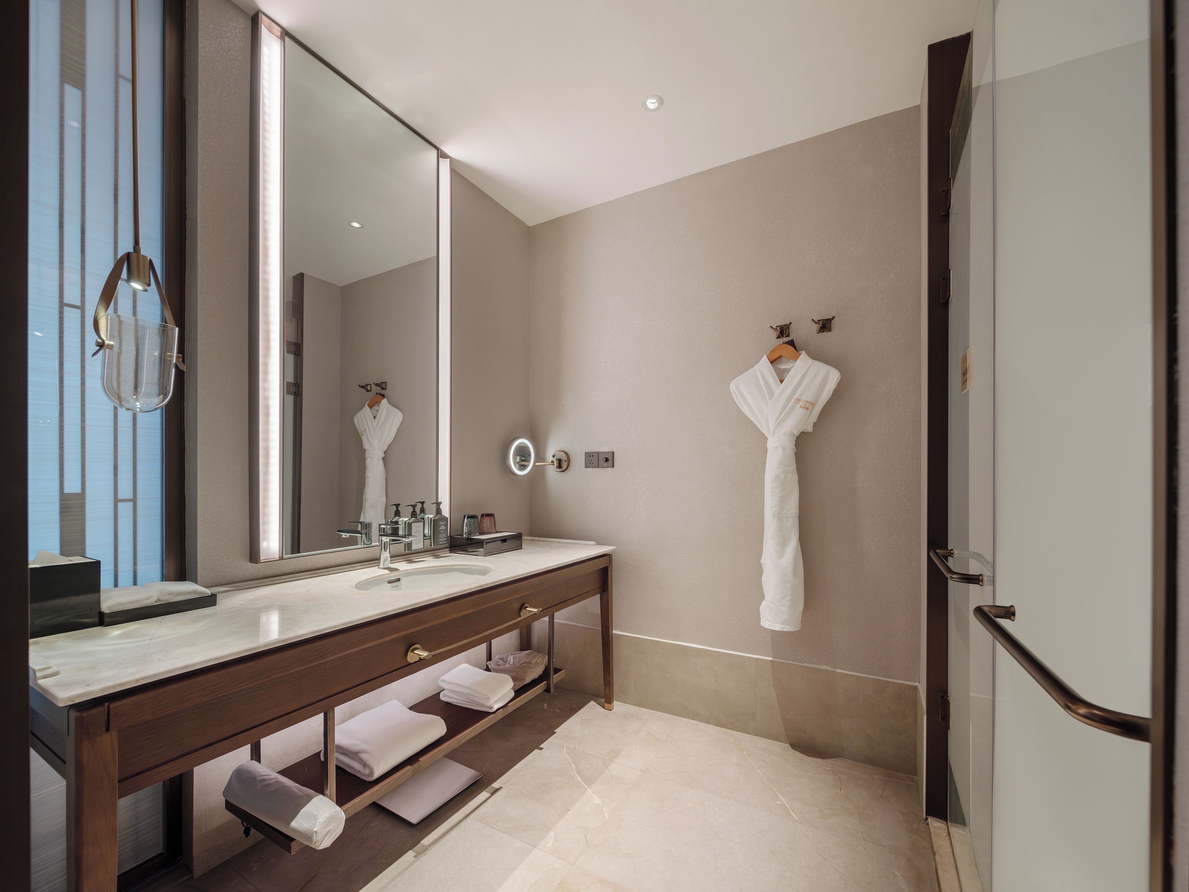Un bagno moderno con uno specchio grande, un mobile lavabo e due accappatoi appesi a dei ganci.