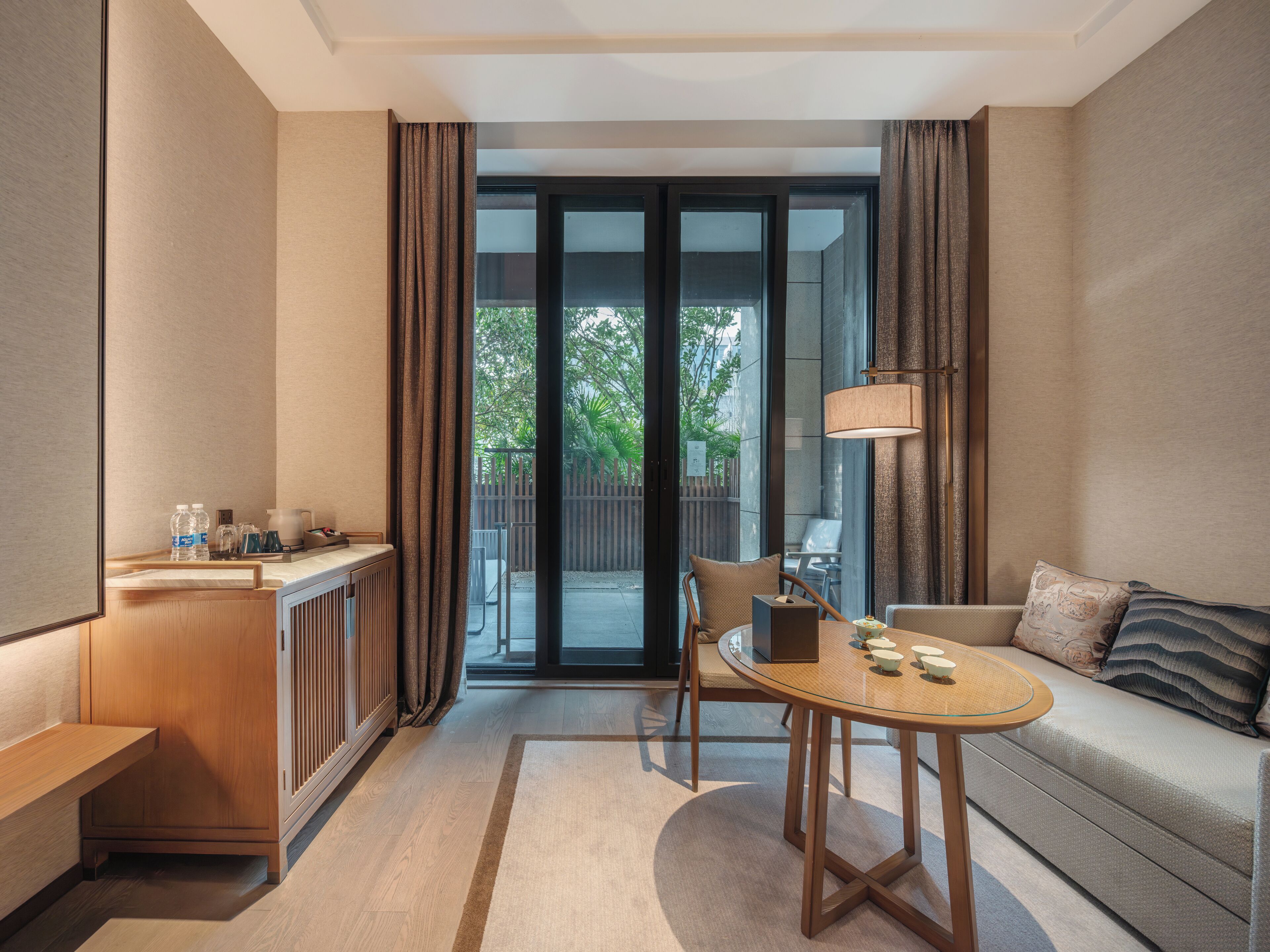 Une chambre d’hôtel moderne avec une kitchenette en bois, une table à manger en verre, un canapé et une vue sur l’extérieur.