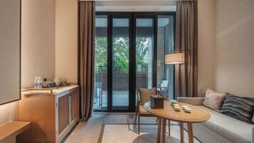 Une chambre d’hôtel moderne avec une kitchenette en bois, une table à manger en verre, un canapé et une vue sur l’extérieur.