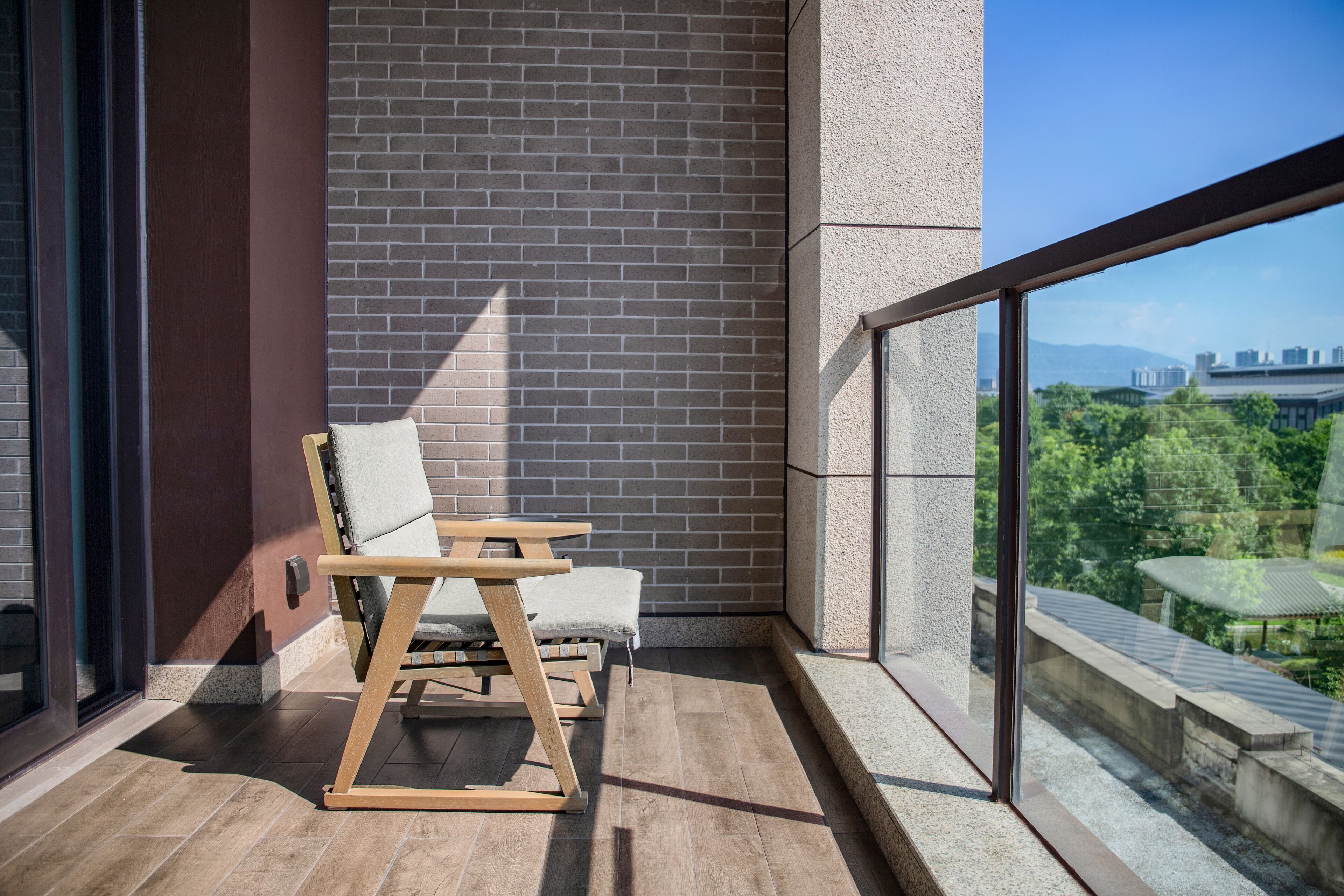 A balcony with a wooden chair and a small table, a brick wall, and a view of a cityscape.
