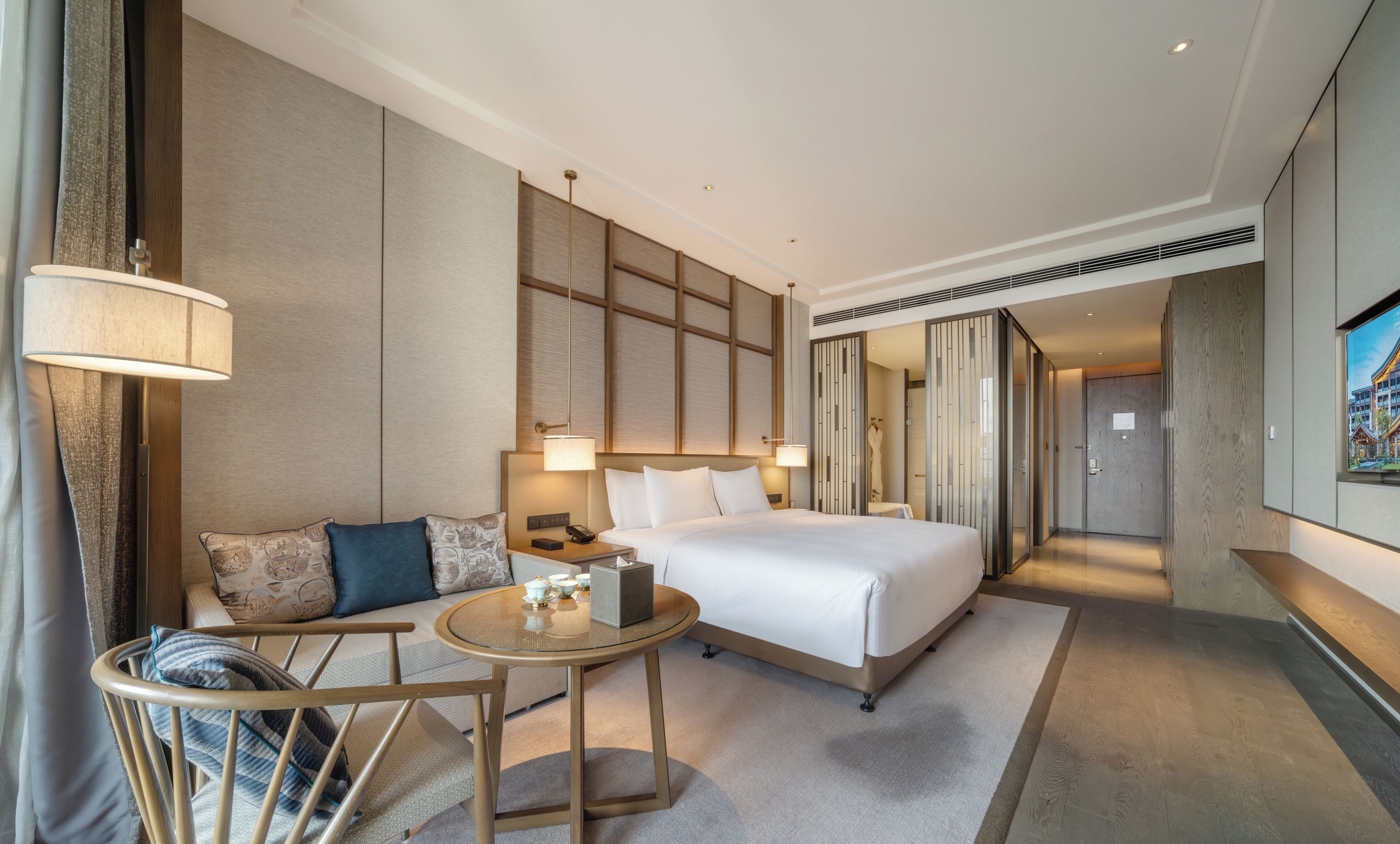 Habitación de hotel con una cama grande, un sofá, una mesita redonda y vistas al exterior.