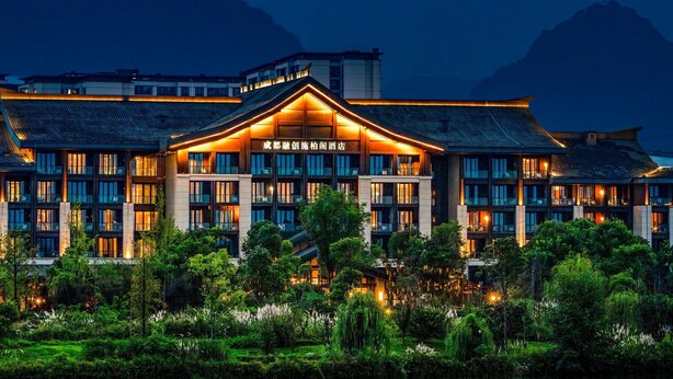 Un hotel dallo stile architettonico tradizionale, con diversi piani e un ingresso ben visibile e illuminato.
