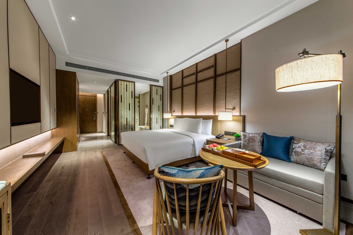 A hotel room with a bed, a sofa, a TV, a desk, and a lamp.