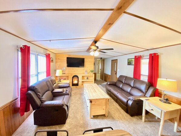 A cozy living room with a fireplace, leather sofas, a wooden coffee table, and a TV mounted on the wall. - 2 bedroom in Logan Ohio, Hocking Hills, Luxury Hot Tub, King Size Bed, Fire-pit (Logan)
