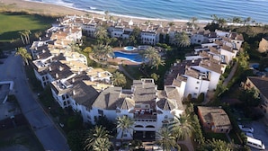 Vista aérea de un resort con varias construcciones, una piscina central y una playa al fondo.