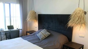 A modern bedroom with a large bed, a desk with a laptop, and two hanging lamps. - Beachfront apartment with sea views. (Estepona)