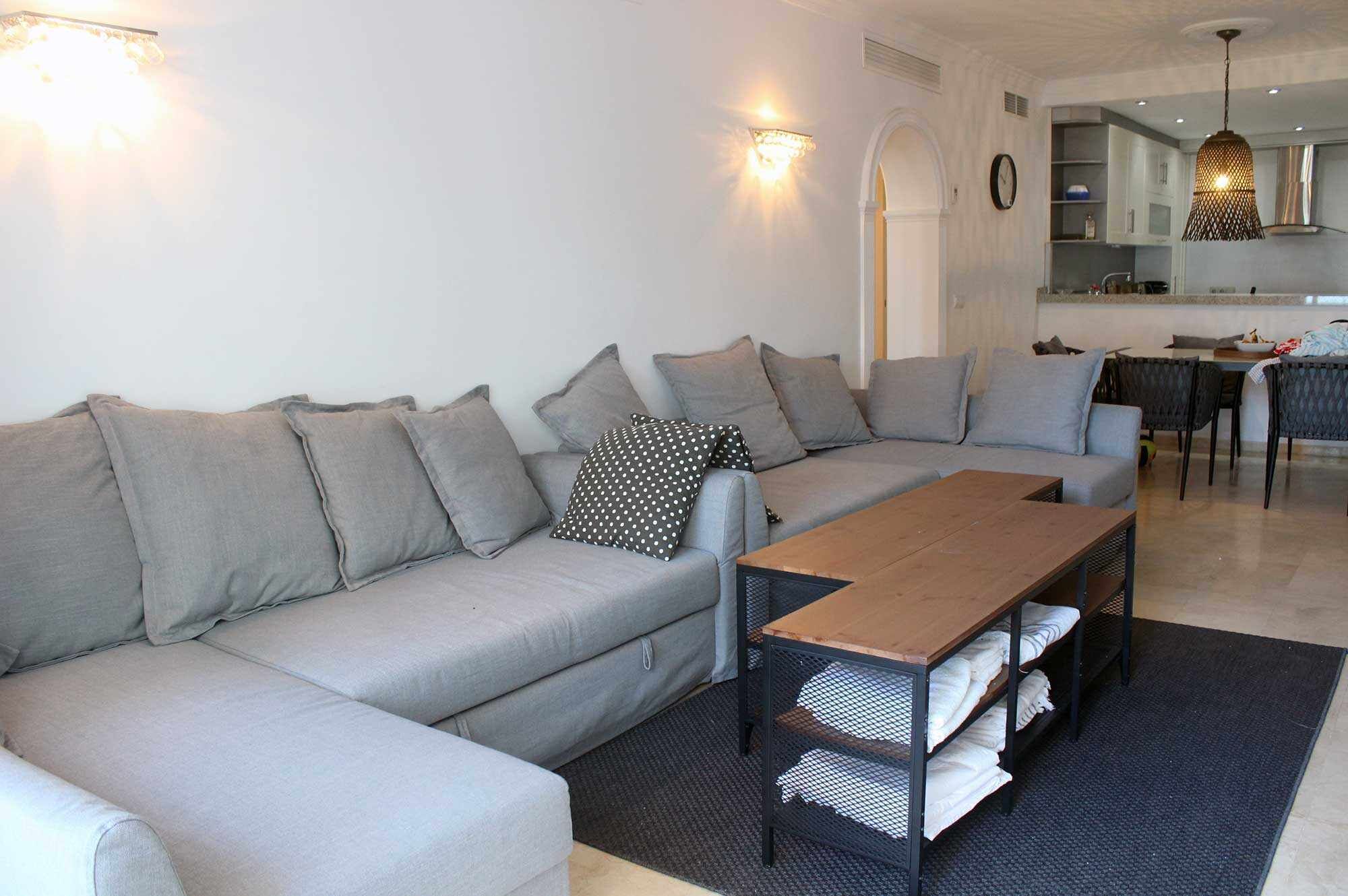 A modern living room with a grey sofa, a wooden coffee table, and a dining area with a table and chairs.
