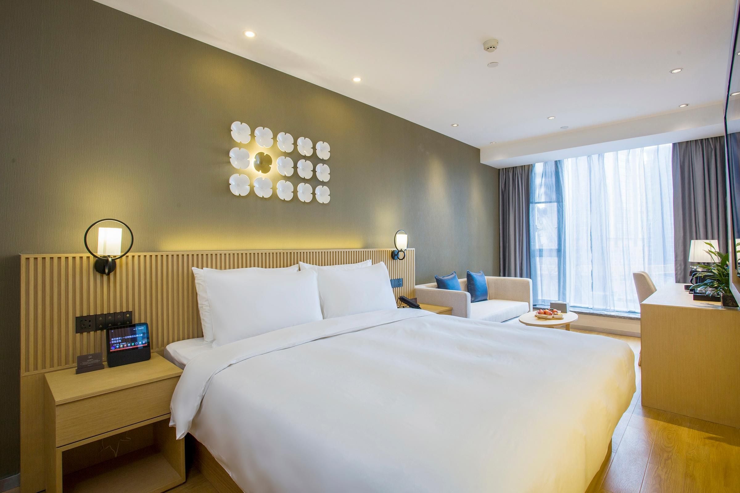 A hotel room with a large bed, two bedside tables, a wall-mounted light fixture, and a window with curtains.