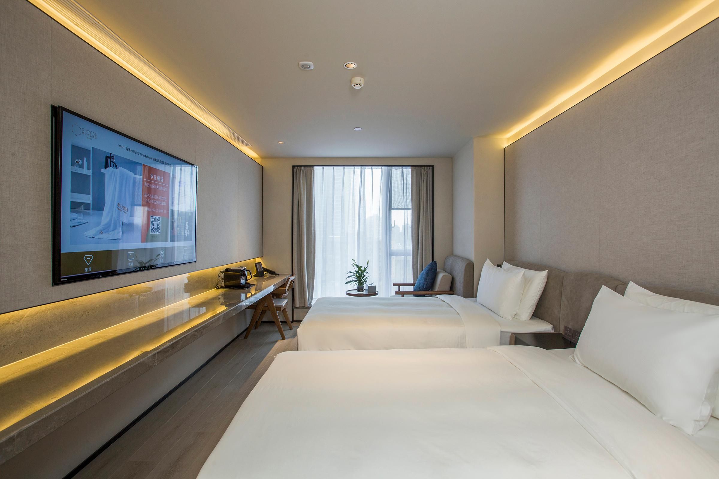 Une chambre d’hôtel avec deux lits, un bureau, un téléviseur fixé au mur et une fenêtre avec des rideaux.