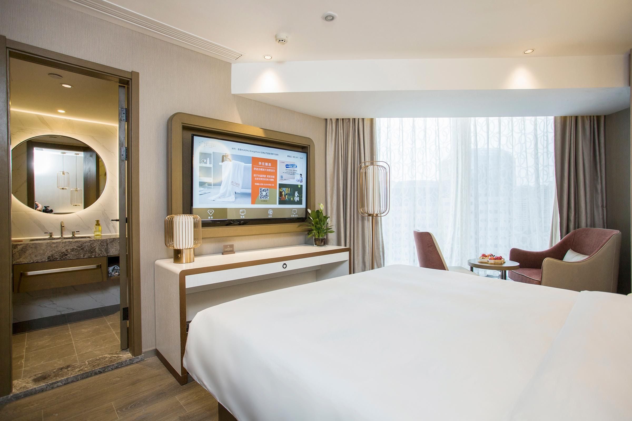 A hotel room with a bed, a desk with a TV, a mirror, a bathroom, and a view of the outdoors.