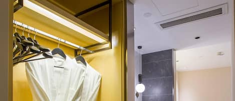 Une salle de bain d’hôtel équipée d’un porte-peignoir, d’un miroir, d’un lavabo avec un plan de travail en marbre et d’un espace douche.