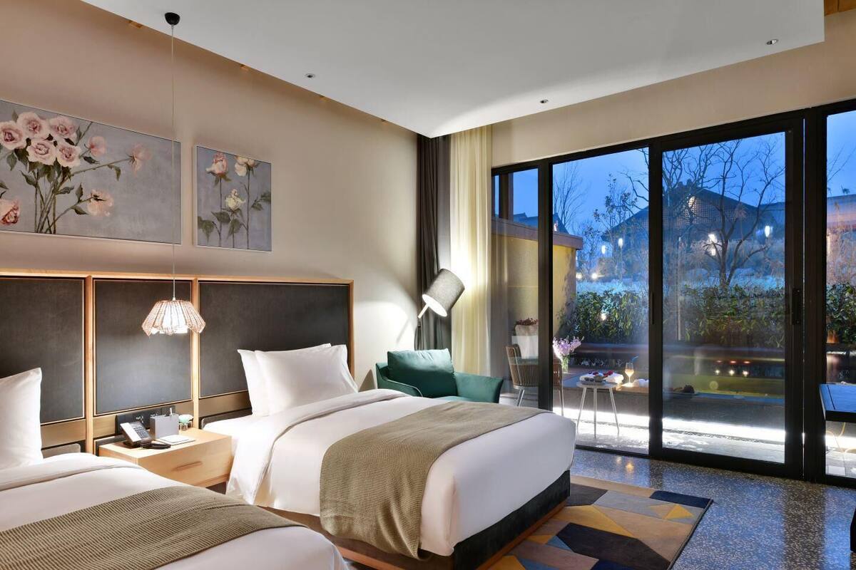 Ein modernes Hotelzimmer mit zwei Betten, einem großen Fenster und Kunstwerken an der Wand.