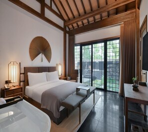 Habitación de hotel con cama, lámparas de noche, un banco, un escritorio y vistas al exterior mediante una puerta corrediza.
